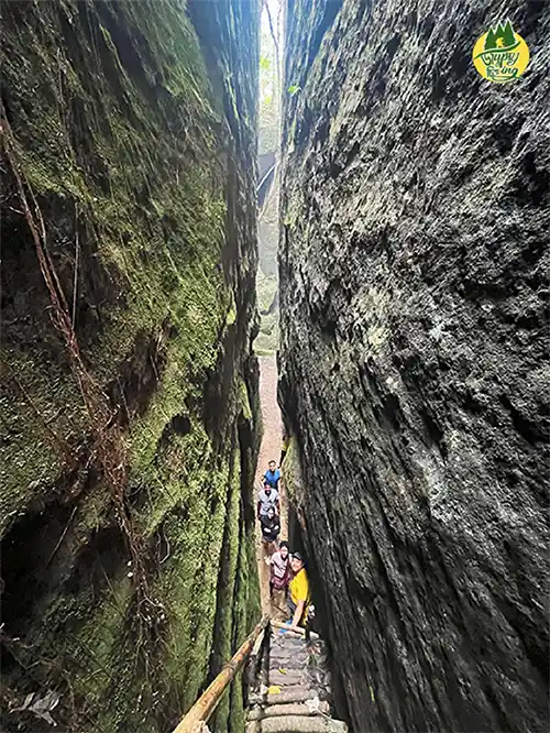 a group of people walking through a narrow canyon - mawlyngbna split rock in meghalaya india