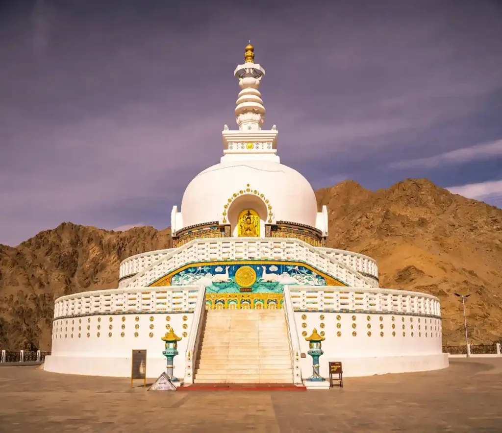 a white pagoda with a steeple and a rocky hill with Shanti Stupa in the background in leh ladakh india