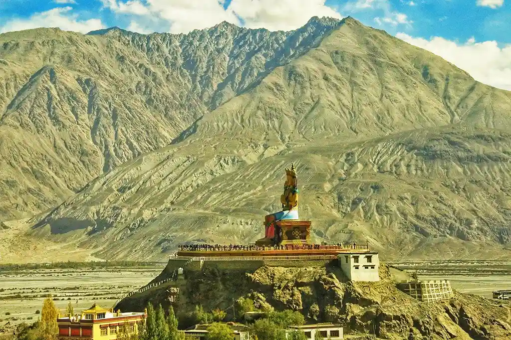 a large statue on a hill with a mountain in the background - View of Diskit, Diksit, Deksit Monastery in Ladakh India