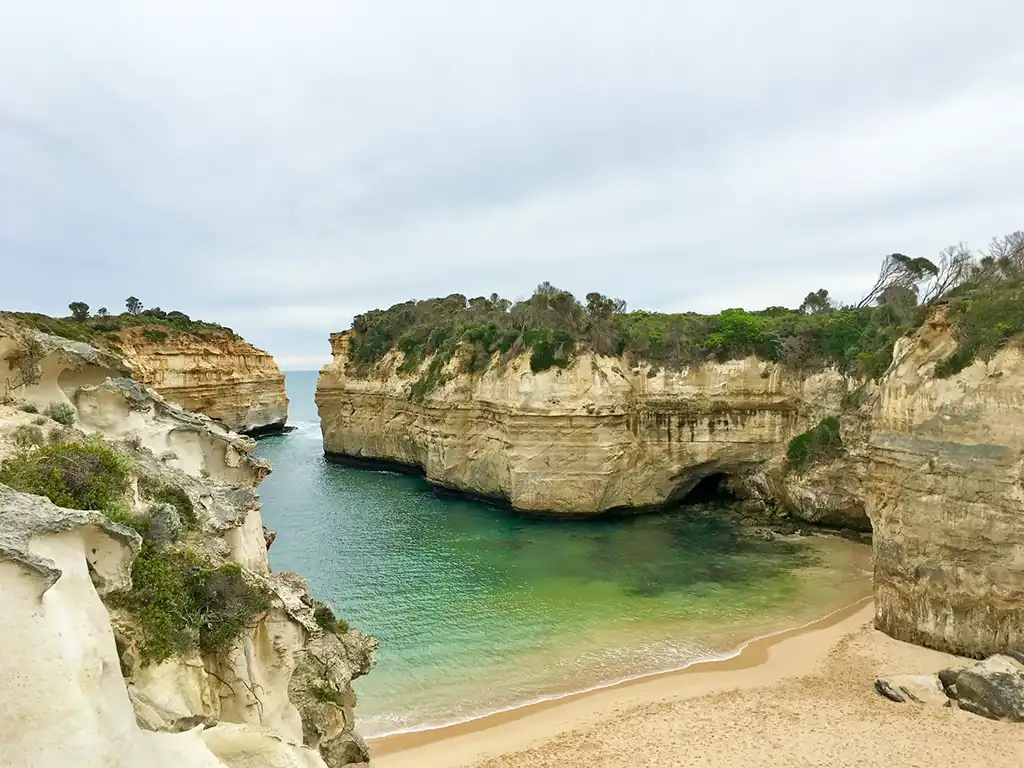 a beach with a cliff and water with Loch Ard Gorge in the background